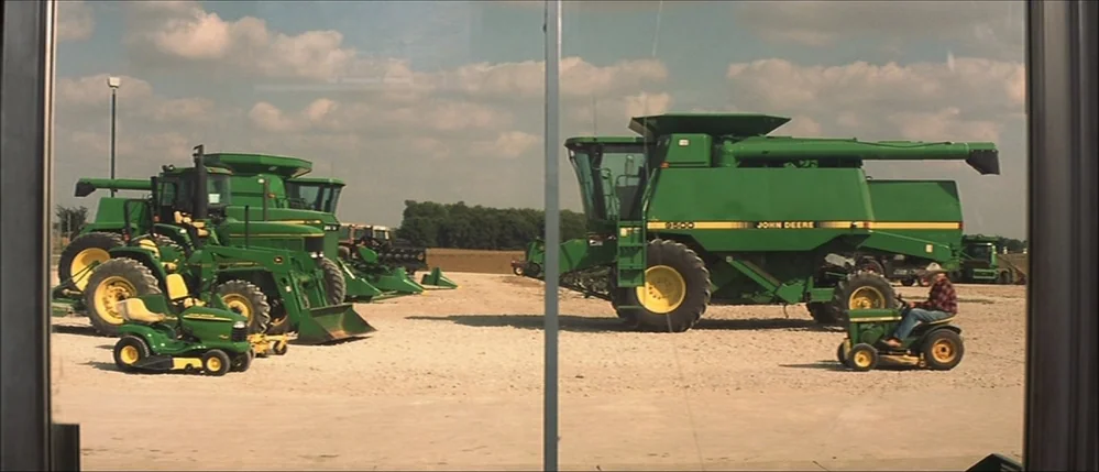 The Straight Story (1999) movie still: wide — A gravel-surfaced commercial lot displays several large John Deere green agricultural combines and…