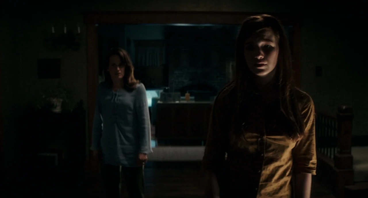 Ouija: Origin of Evil (2016) movie still: medium — A dimly lit indoor hallway connects two residential living areas in near-total darkness. Two…