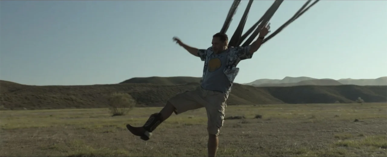 Venom: The Last Dance (2024) movie still: fullbody — A vast, dry desert landscape stretches out beneath a clear, pale daytime sky. A man in cargo…