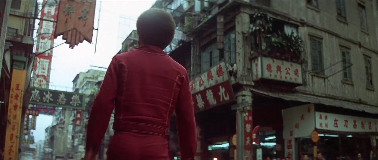 Enter The Dragon (1973) movie still: fullbody — A dense urban street in Hong Kong with many signs in Chinese characters. A man with a prominent afro…