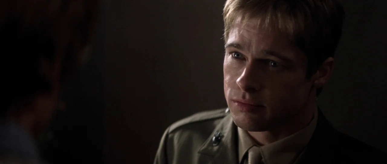 Spy Game (2001) movie still: medium — A dimly lit room with dark walls obscured by deep shadows. A man in military uniform looks toward a person…