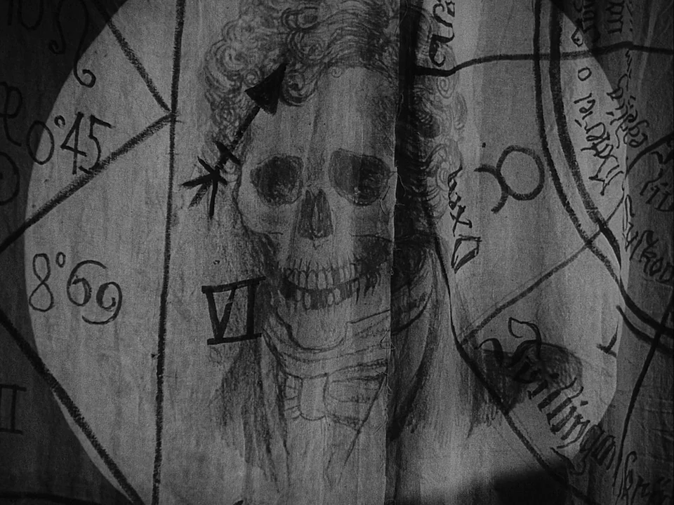 The Magician (1958) movie still: closeup — A piece of wrinkled fabric displays a detailed charcoal drawing of a skull. Handwritten astrological…
