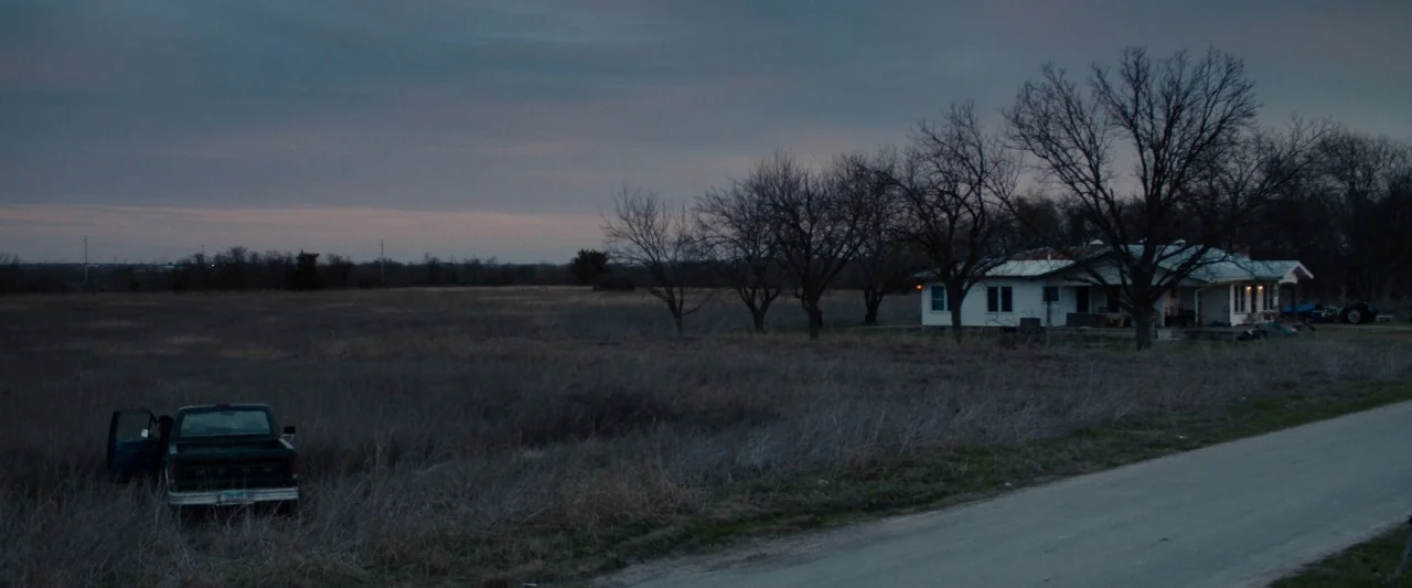 Little Woods (2018) movie still: wide — A rural landscape features a white house among barren trees and a parked truck. The vehicle remains stopped…