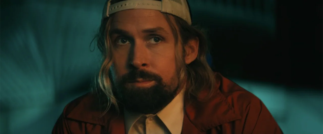 The Fall Guy (2024) movie still: closeup — A man sits in a dark, dimly lit environment with teal shadows. The subject faces the camera while wearing…