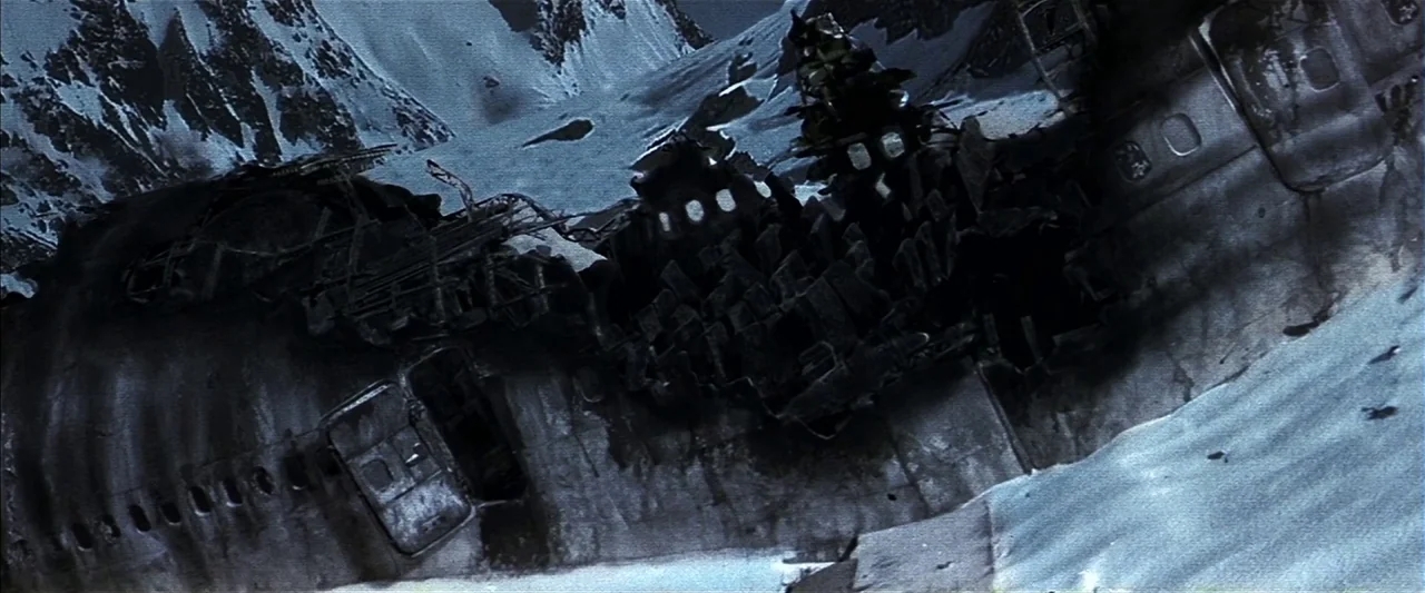 A wreckage of a large commercial aircraft lies partially buried in a snowy mountainside. The mangled fuselage is torn open, revealing interior structural ribs against steep snow-covered peaks.