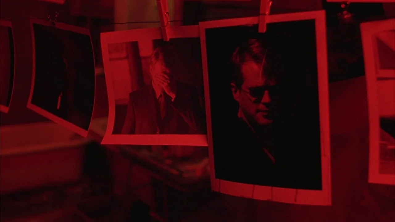 Saw movie still: closeup — Several developed photographic prints hang from a clothesline in a darkroom. The photographs display images of men under…