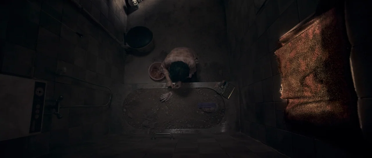 Rigor Mortis (2013) movie still: wide — A dark, tiled room features a recessed basin filled with dirt and debris. A person kneels by the basin,…