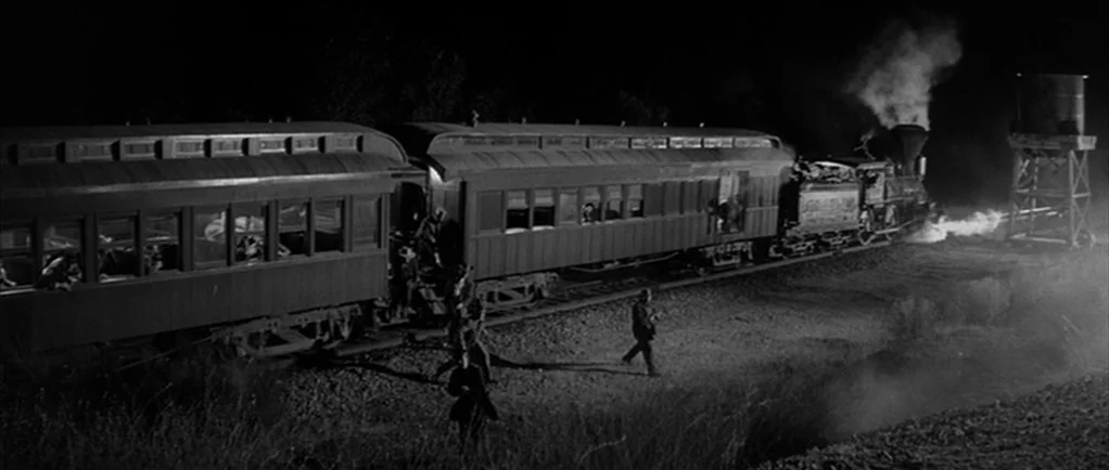 Love Me Tender movie still: wide — A steam locomotive and passenger cars are stopped at night on remote desert terrain. Several figures walk along…