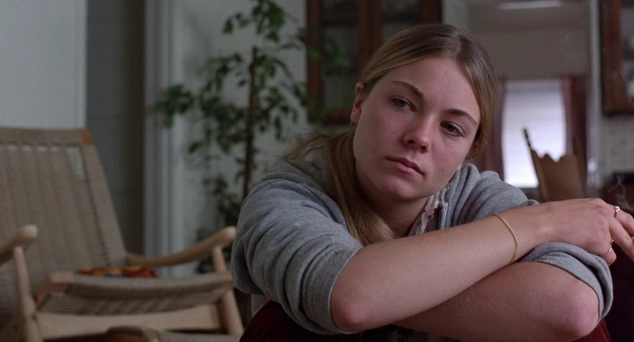 Straight Time (1978) movie still: medium — A residential room features a wooden chair and a potted plant in the background. A young blonde woman in…