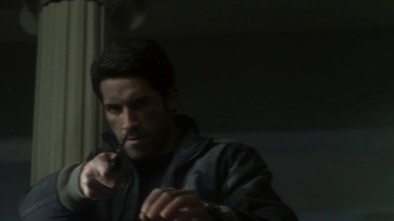 The Shepherd (2023) movie still: medium — A dimly lit indoor corridor with a visible structural column in the background. A man in a dark jacket…
