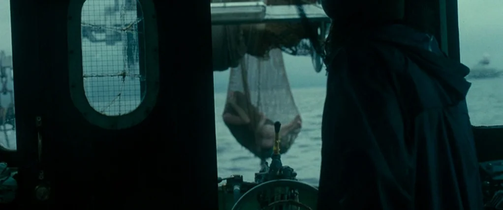 Ondine (2009) movie still: medium — An interior view looking from a dark boat cabin out towards a grey ocean. A person is inside looking at a nude…