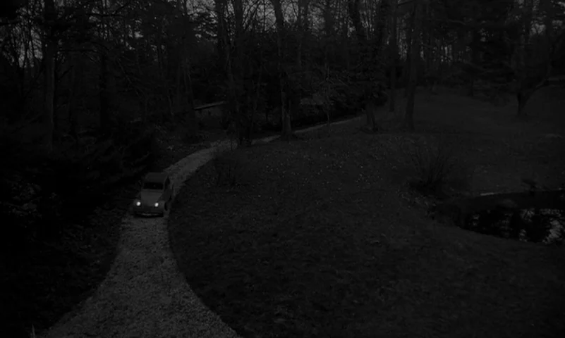 Eyes Without A Face (1960) movie still: wide — A dark, winding gravel driveway cuts through a wooded park area at night. A lone vehicle drives along…