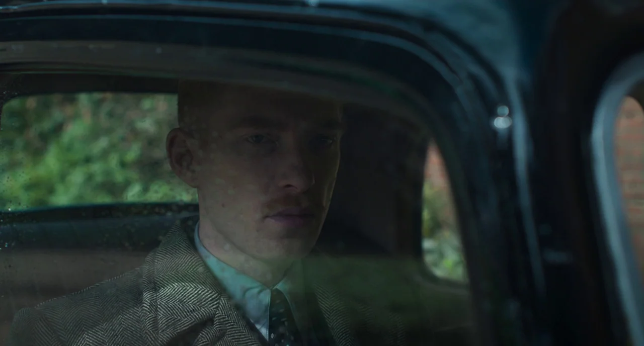 The Little Stranger (2018) movie still: medium — A man sits inside the passenger seat of a vintage automobile with raindrops visible. He looks ahead…