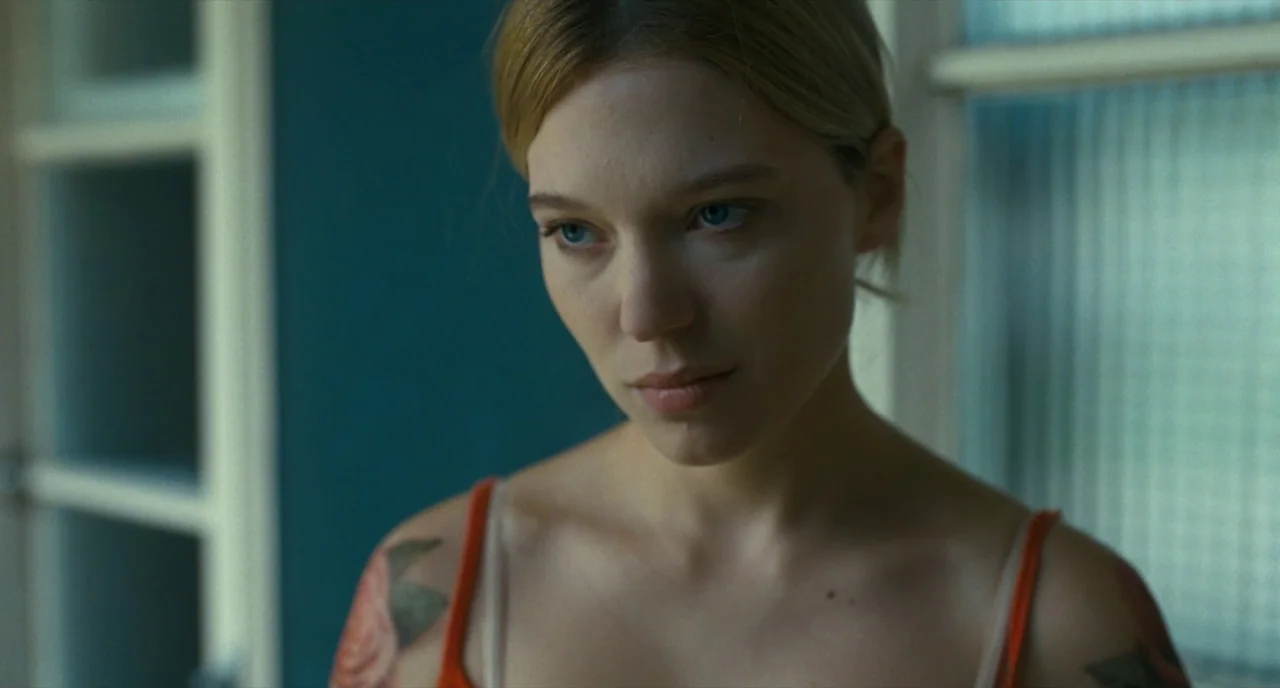 It’s Only The End Of The World (2016) movie still: closeup — A woman stands indoors near a teal wall and a window with translucent glass. She is…