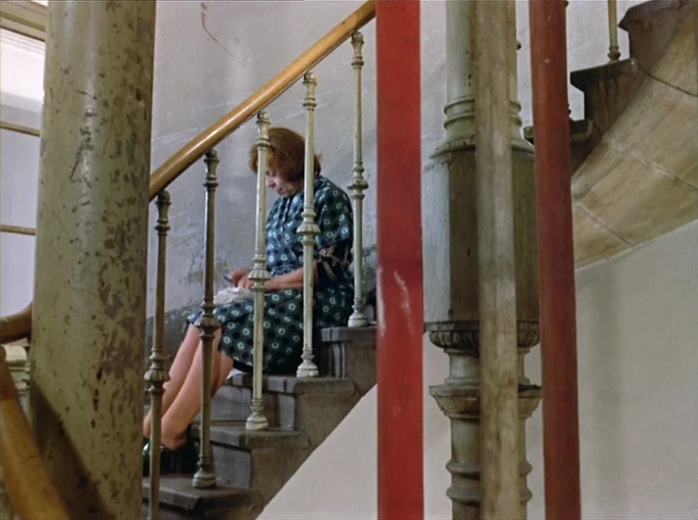 Ali: Fear Eats The Soul (1974) movie still: medium — An interior stone staircase features ornate metal railings with a wooden handrail. A woman in a…