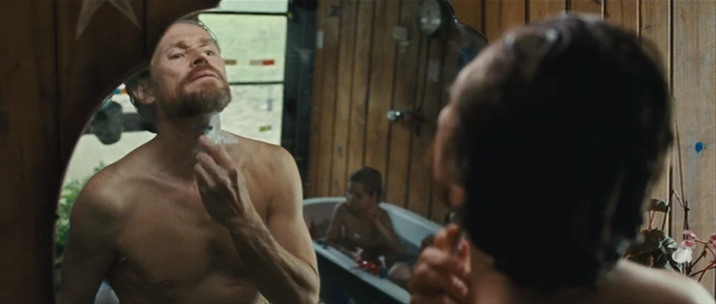 The Hunter (2011) movie still: medium — A rustic wooden-paneled bathroom with a wall mirror reflecting a man and bathtub. A man stands before the…