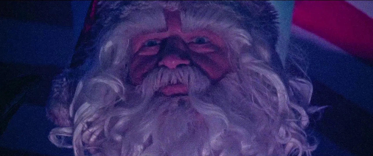 Christmas Bloody Christmas (2022) movie still: closeup — A dark indoor space is lit by intense blue and magenta colored lights. A man dressed as…