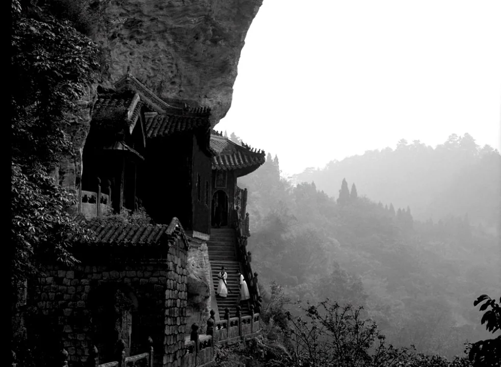 The Assassin (2015) movie still: wide — A historic temple is built directly into a jagged cliff face overlooking a misty valley. Two figures in…