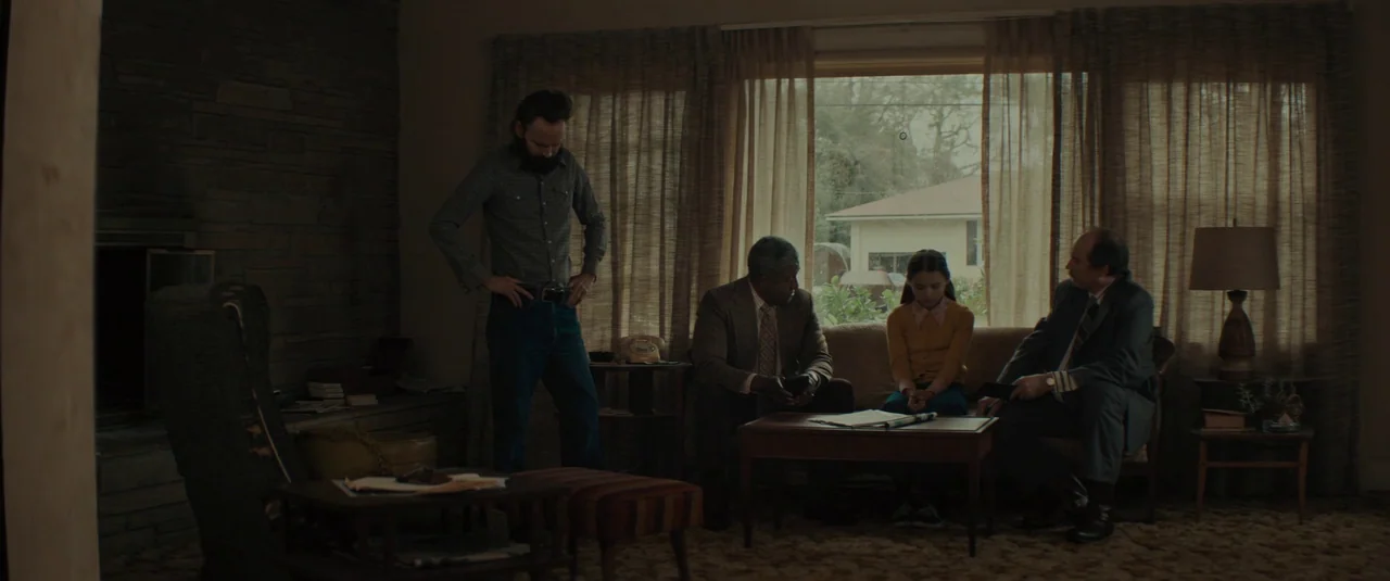 The Black Phone (2021) movie still: wide — A 1970s living room features stone fireplace cladding, shag carpeting, and wood-paneled walls. Four…