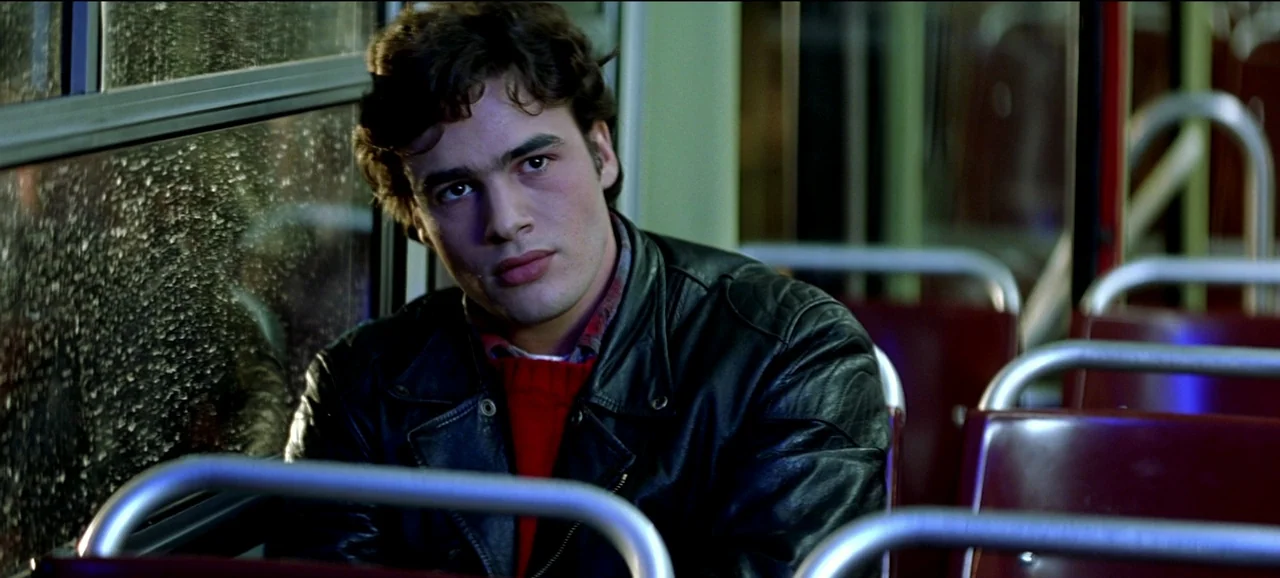 Live Flesh (1997) movie still: medium — A dark bus interior at night with rain streaks visible against the window glass. A young man sits in a…