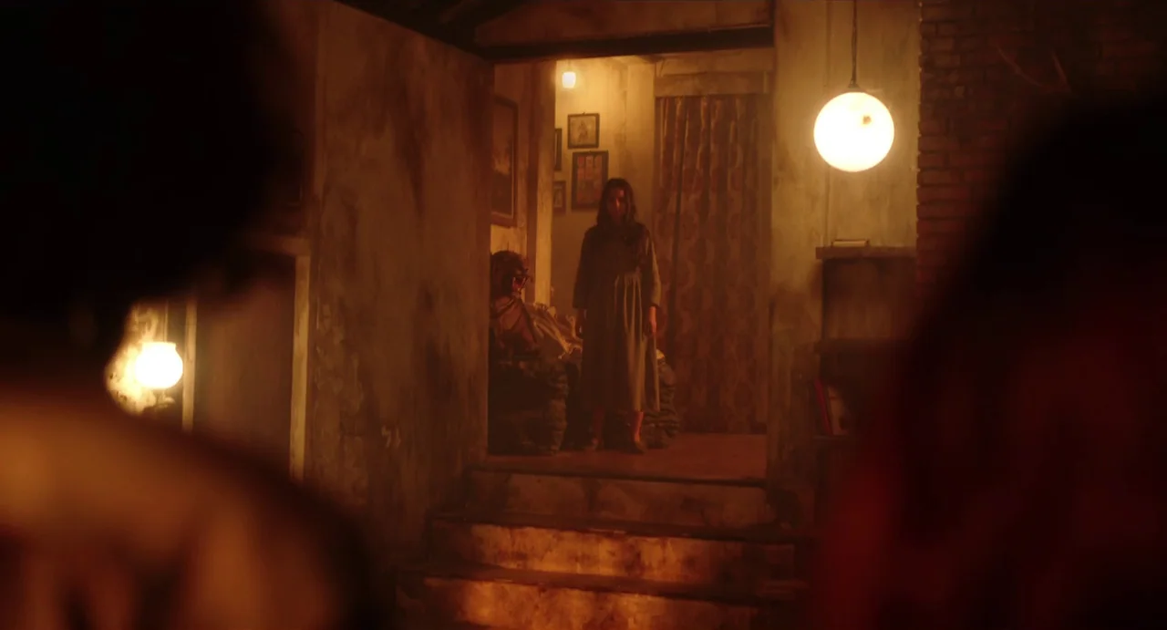 May The Devil Take You (2018) movie still: medium — A dimly lit, weathered space with peeling walls and a small staircase. A woman stands in the…