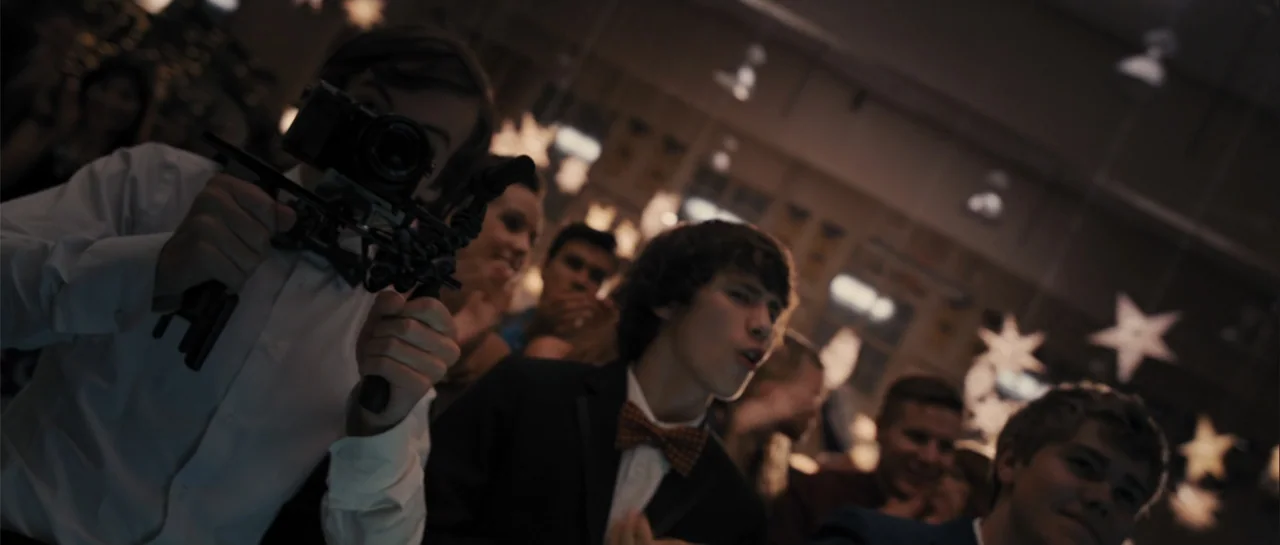 Carrie (2013) movie still: medium — A school gymnasium features hanging star decorations and crowded groups of teenagers. One student in a white…