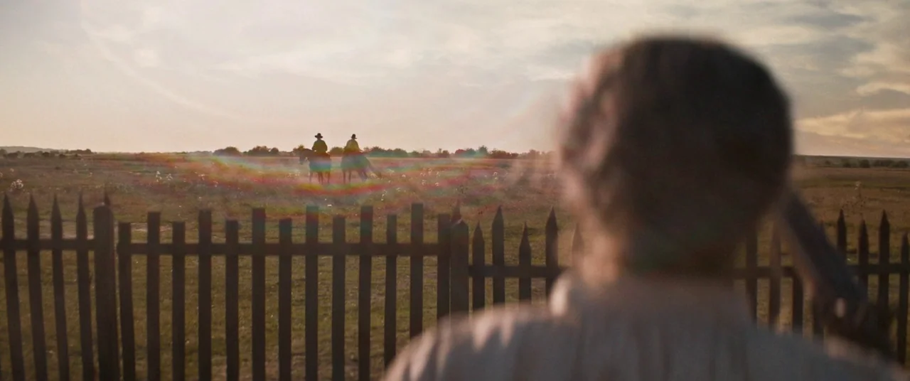The Sisters Brothers (2018) movie still: wide — An open grassy field stretches into the distance under a pale golden hour sky. Two small figures on…