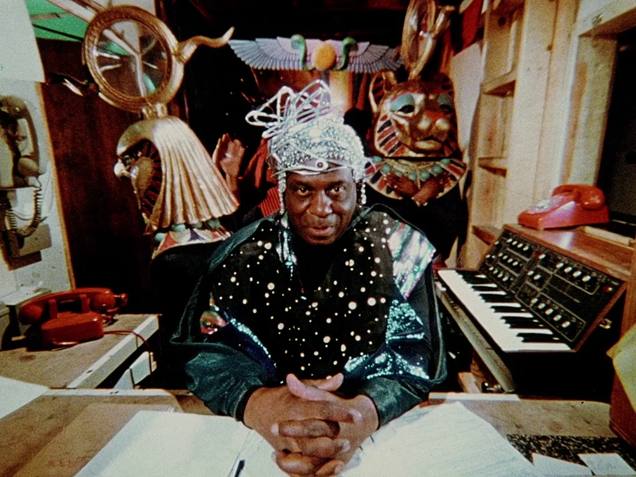 Space is the Place (1974) movie still: medium — An eccentric studio space contains vintage analog synthesizers, red telephones, and large…