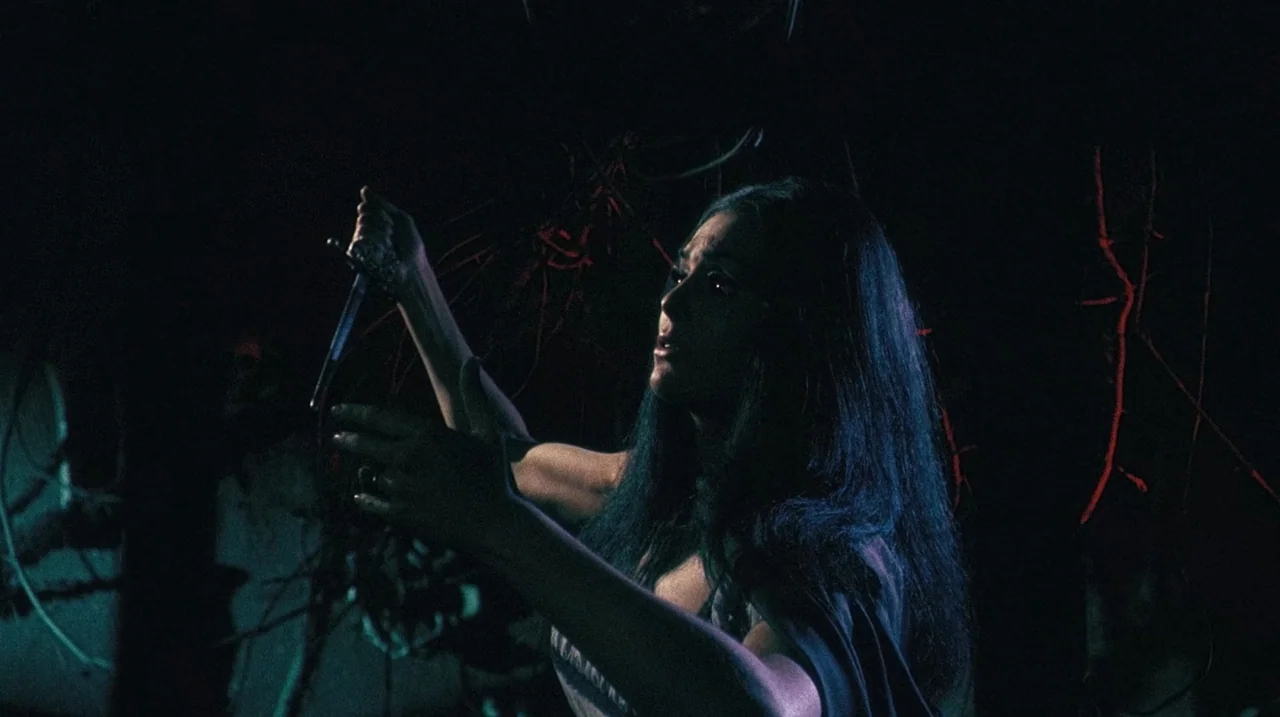 The Whip and The Body (1963) movie still: medium — A dark night forest with twisted red branches visible in the background. A woman holds a small…