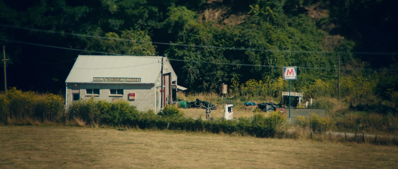 Z for Zachariah (2015) movie still: establishing — A small rural drive-in market with an attached gas pump sits in a field. Lush green vegetation…
