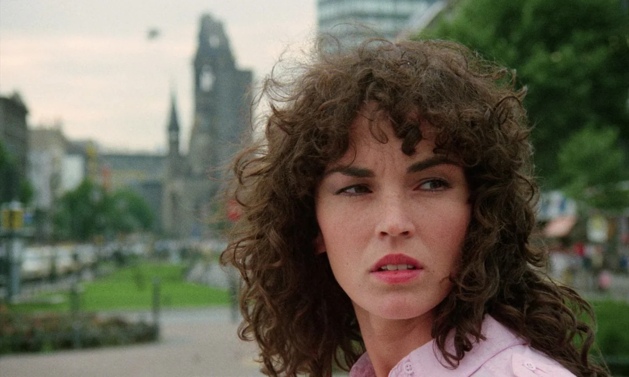 Demons (1985) movie still: closeup — A woman stands in a city square in front of a distant damaged church tower. She turns her head and looks toward…