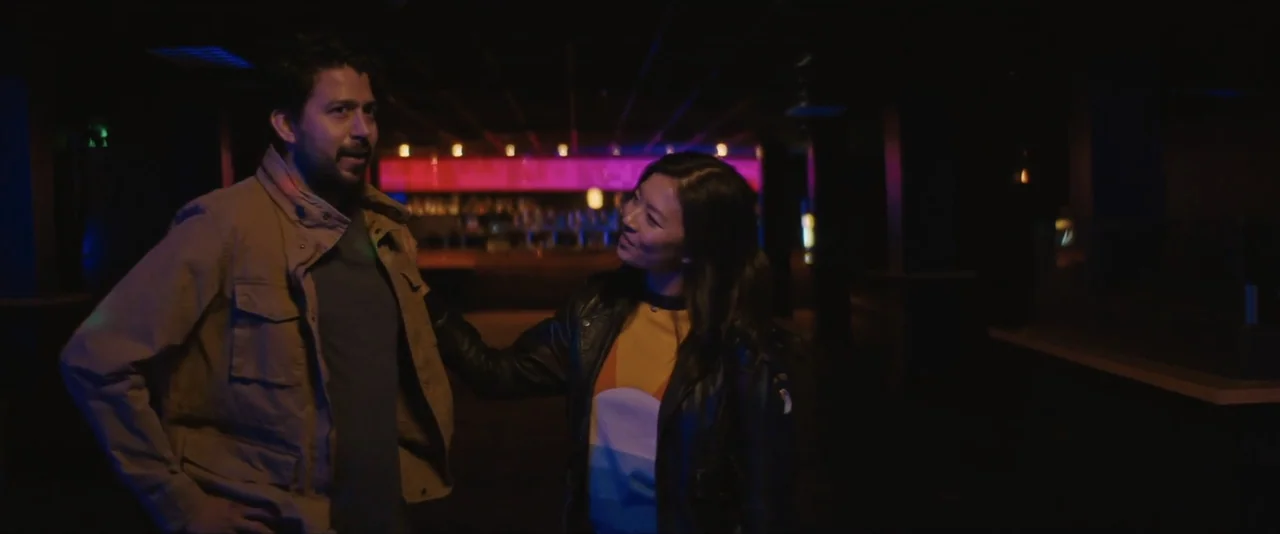 Stalker (2020) movie still: medium — A dimly lit bar interior features rows of dark booths and a distant glowing bar. A man and a woman stand…