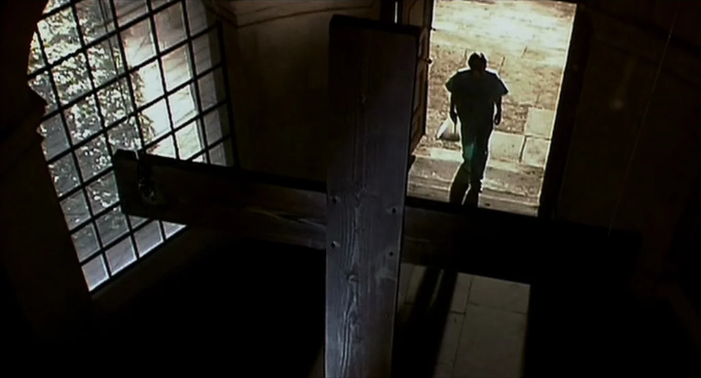 28 Days Later (2002) movie still: wide — A dark church interior with a large wooden cross looming in the foreground. A lone man walks from the…