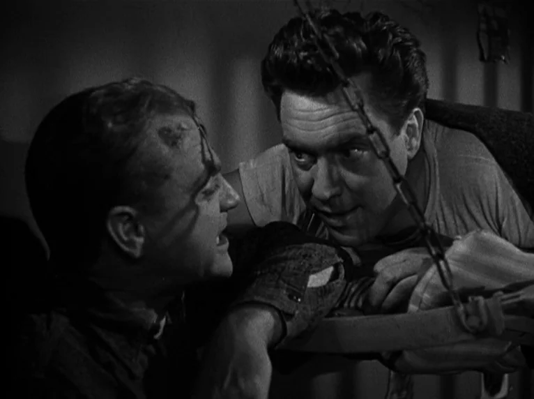 White Heat (1949) movie still: medium — Two men interact in a dimly lit, narrow metal space resembling a detention unit. They lean toward each other…