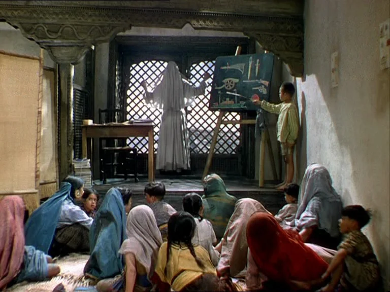 Black Narcissus (1947) movie still: wide — A sparsely furnished room contains a teacher standing by a window and students seated. A young boy stands…
