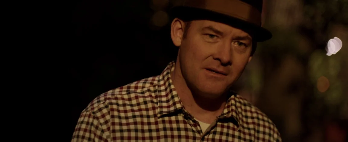 Cheap Thrills (2013) movie still: closeup — A man in a hat stands in a dark outdoor setting at night. He faces slightly right while looking away…