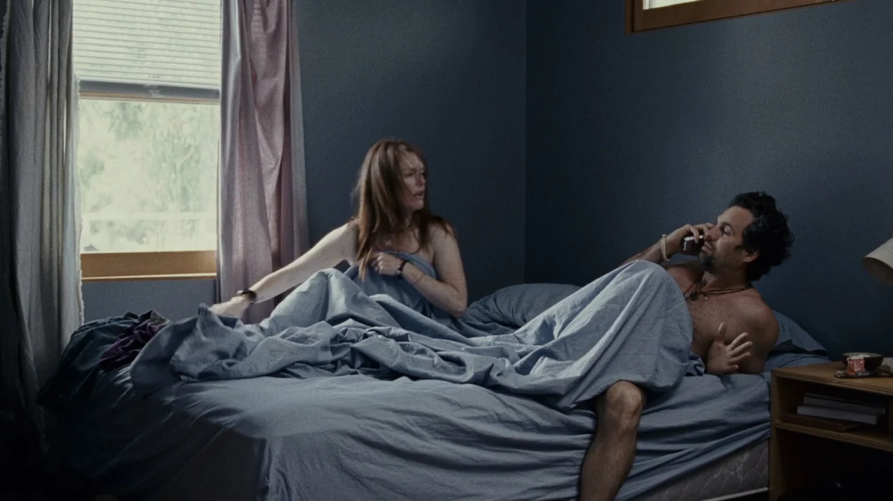 The Kids Are All Right (2010) movie still: medium — A bedroom with dark blue walls, a wooden nightstand, and a window with curtains. A man and woman…