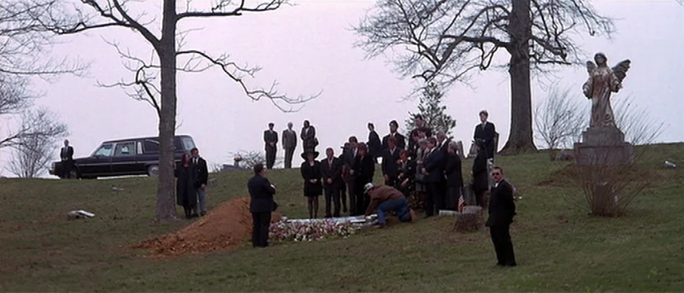 The People vs. Larry Flint (1996) movie still: wide — A grassy cemetery with leafless trees and a stone angel statue in the background. A group of…
