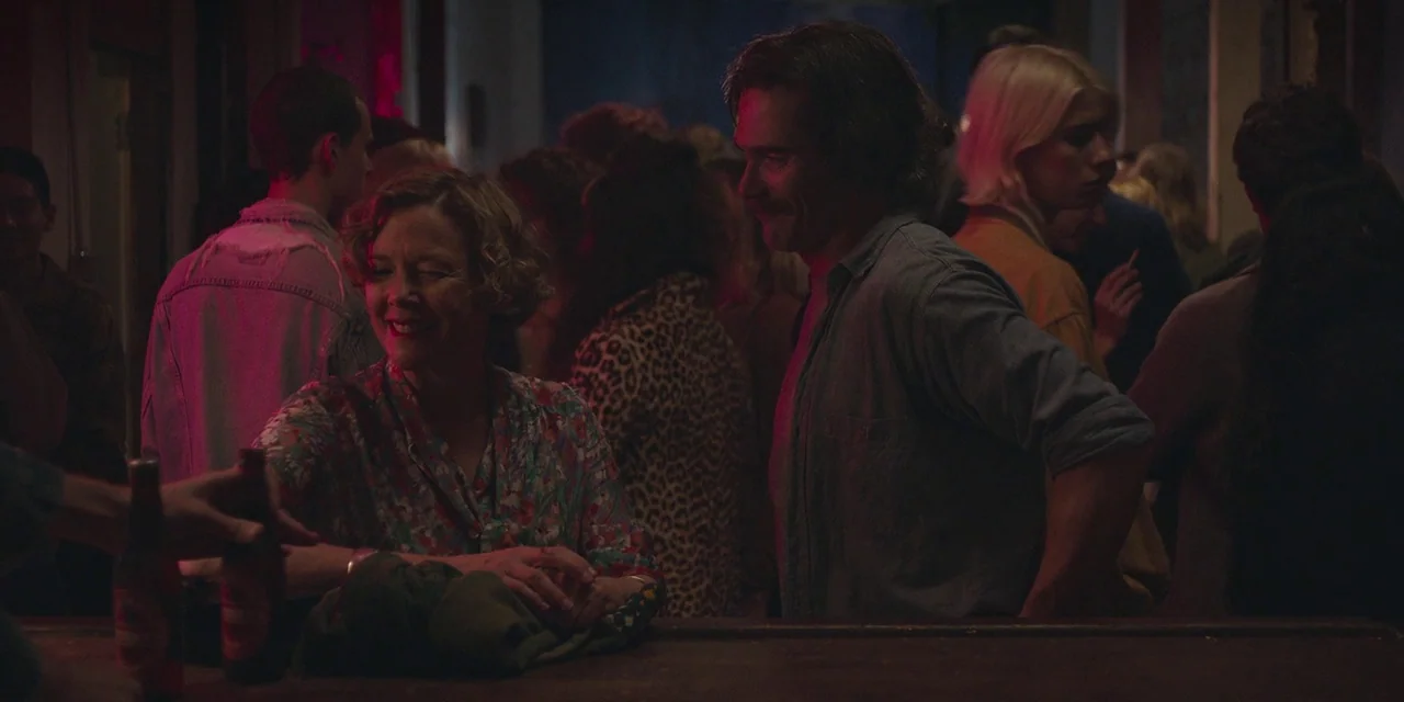 20th Century Women (2016) movie still: medium — A crowded bar interior at night features patrons standing near a dark wooden counter. An older woman…