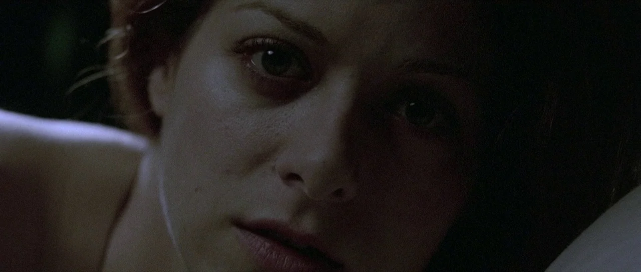 The Mothman Prophecies (2002) movie still: closeup — A dark, dimly lit indoor space at night. A woman is positioned low in the frame looking…