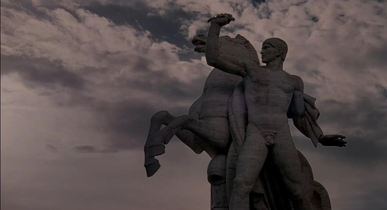 Pasolini (2014) movie still: fullbody — A stone sculpture of a man and a horse sits against an overcast sky. The figure holds the horse's bridle as…