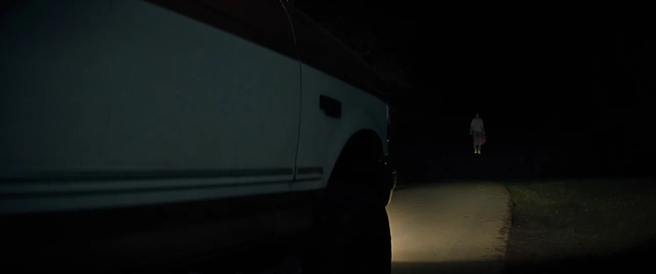 Brightburn (2019) movie still: wide — A dark, paved road is illuminated by a singular beam of light at night. A small child floats in the middle of…