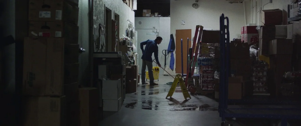 The Rider (2017) movie still: wide — A cluttered storeroom features stacked cardboard boxes lining the walls and a central concrete path. A man…