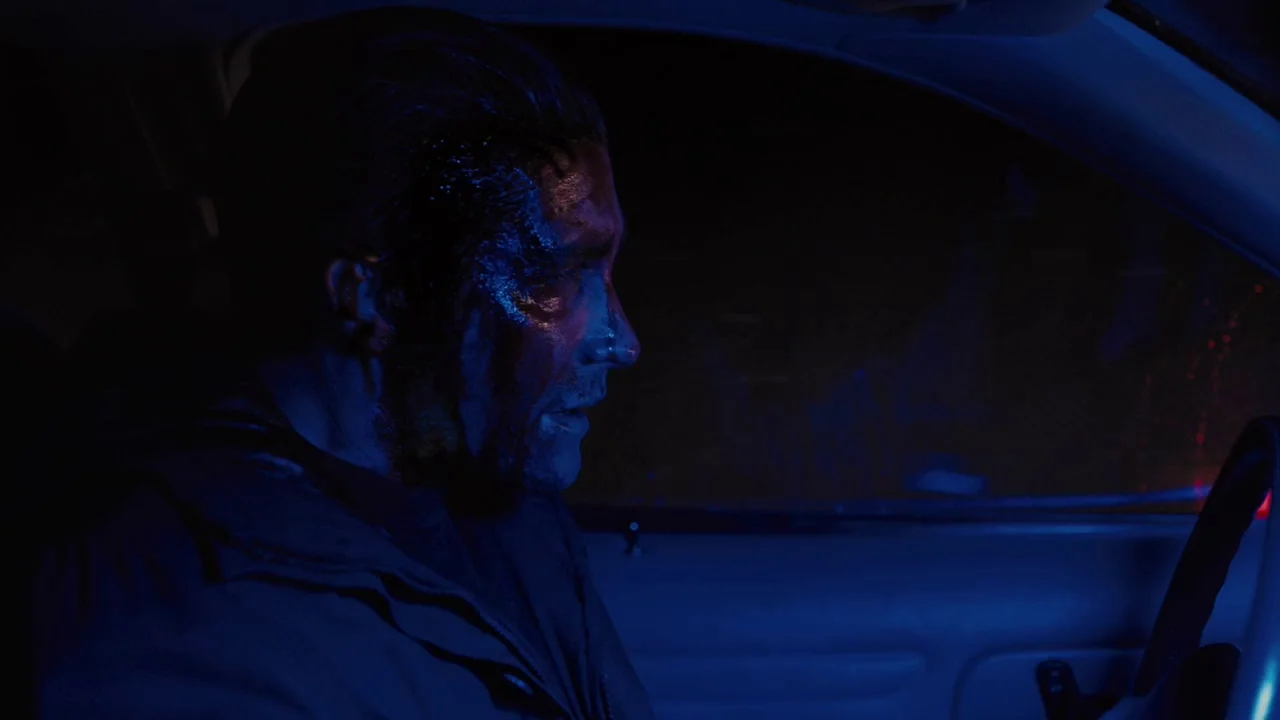 Prisoners (2013) movie still: medium — An interior of a vehicle at night is bathed in heavy blue light. A man sits in the driver seat looking…
