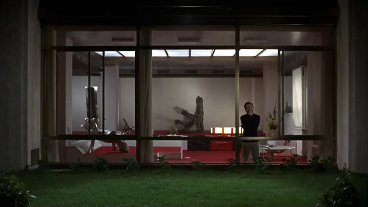 A Quiet Place In The Country (1968) movie still: wide — A spacious modernist house interior features red carpeting and white walls at night. A man…