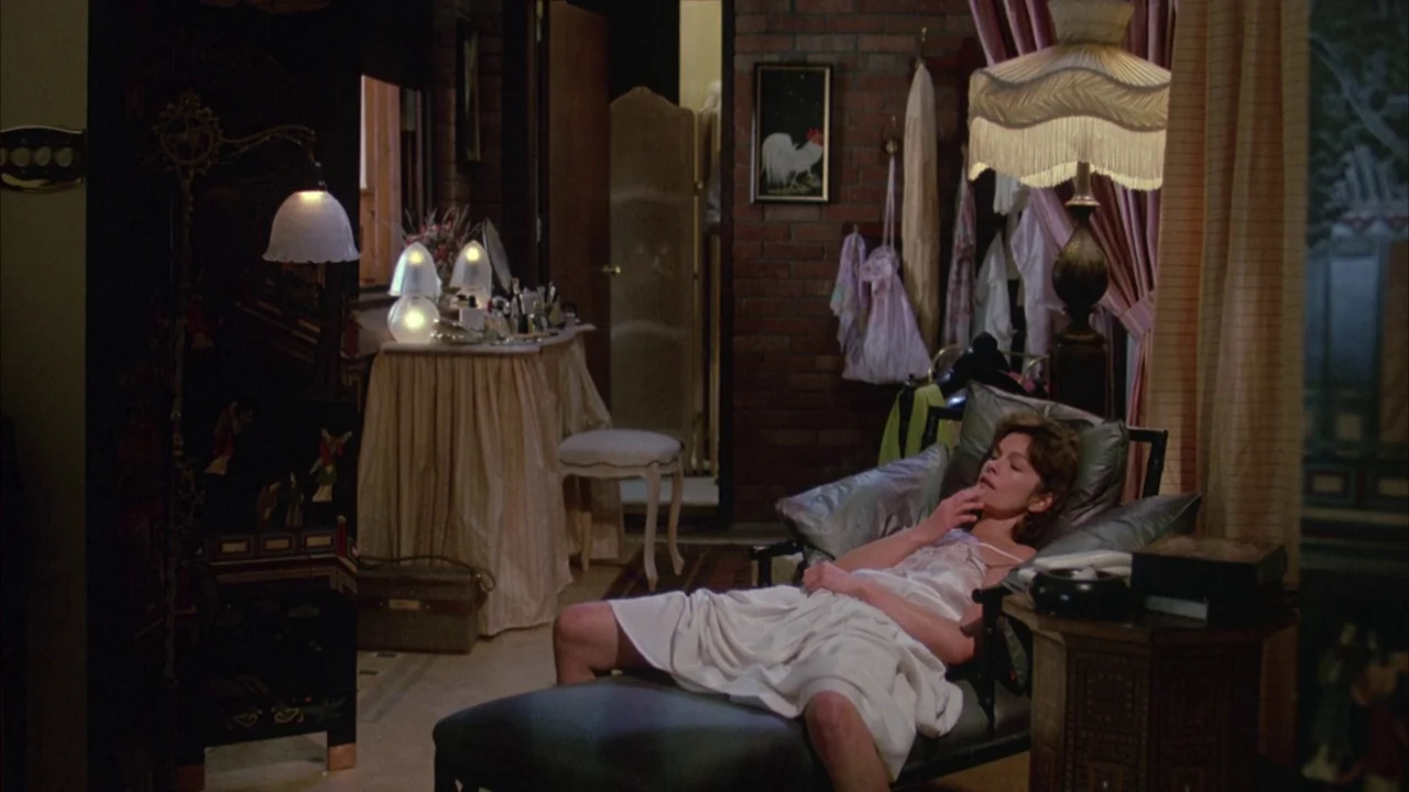 Dead Ringers (1988) movie still: medium — A furnished interior space features a brick wall, ornate lamps, and a vanity table. A woman in a white…