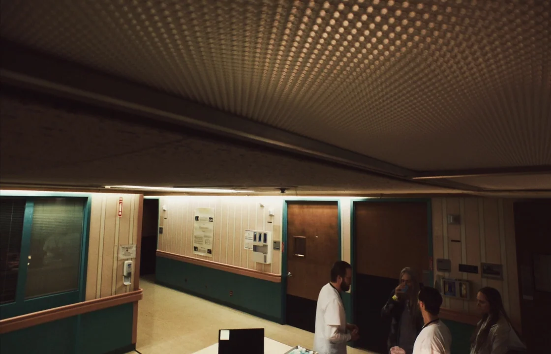 Unsane (2018) movie still: wide — A quiet hospital corridor with green lower wall panels and beige striped wallpaper above. Four individuals stand…
