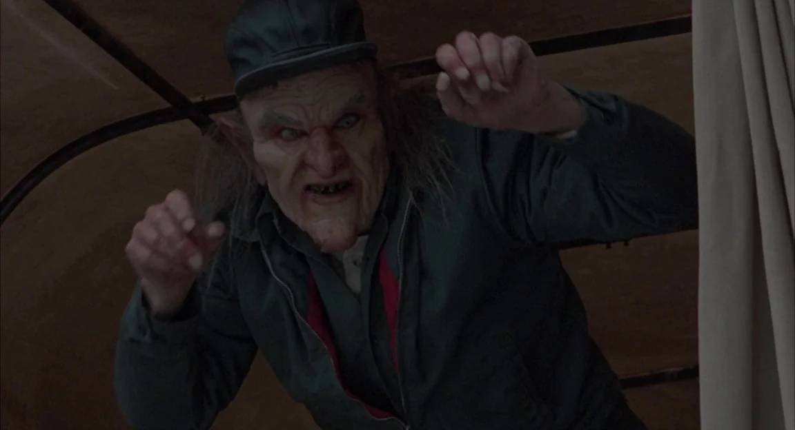 Creepshow 2 (1987) movie still: medium — A dark, cramped interior space defined by curved wooden or metal structural supports. A creature with sharp…