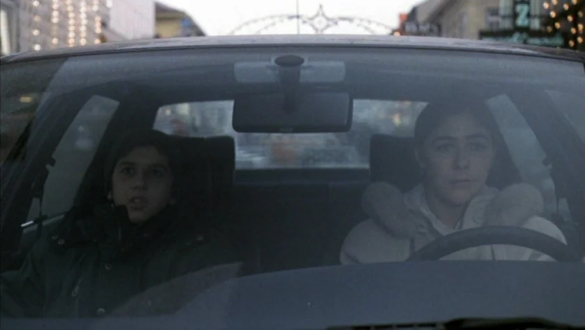 71 Fragments of a Chronology of Chance (1994) movie still: medium — An interior shot looking at two people seated in the front of a car. Through the…
