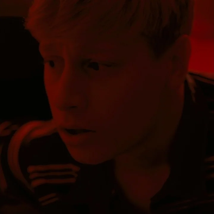 Mommy (2014) movie still: closeup — A man's face is illuminated in a dark room by intense red light. He stares off-camera with a wide-eyed,…